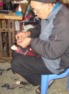 The Red Dzao doll-maker wrapping the man doll’s turban.