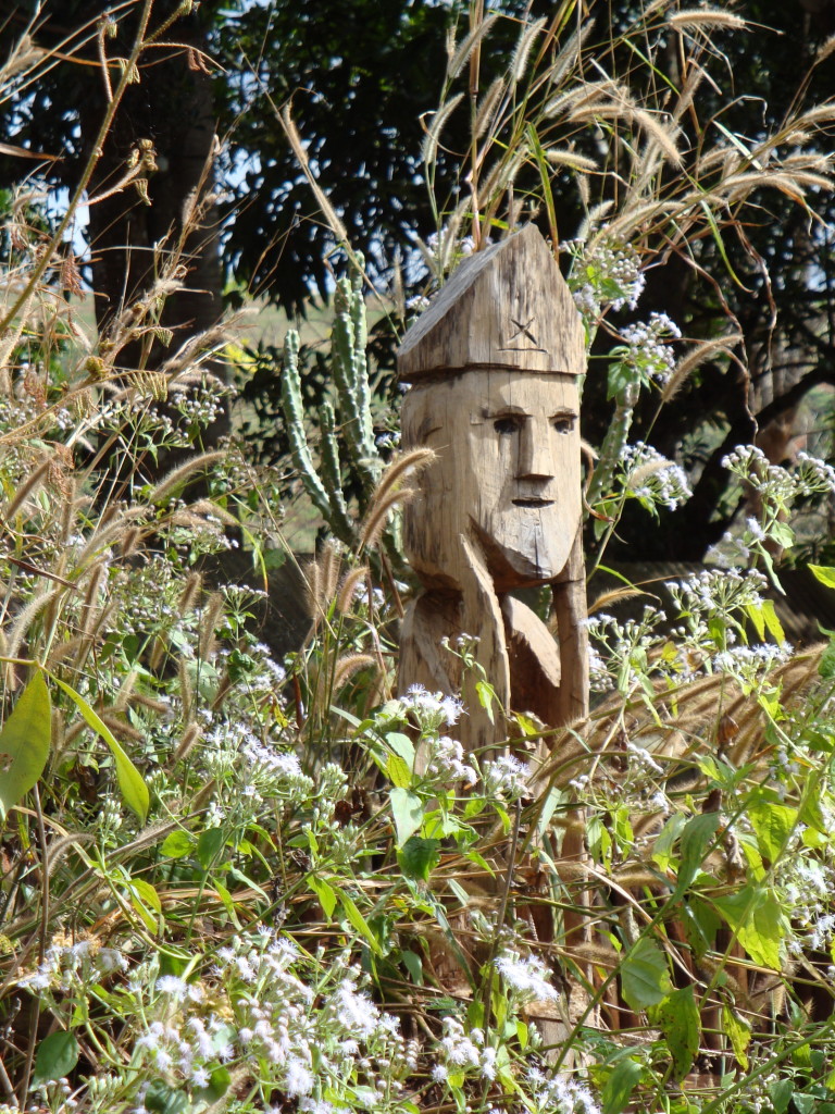 A Jarai guardian of a grave peers over the grass.